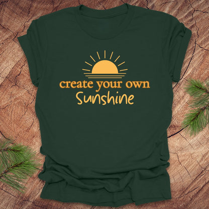Green t-shirt with 'create your own sunshine' text and sun graphic on a wooden surface.