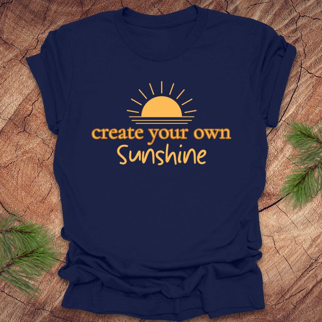 Navy blue t-shirt with 'create your own Sunshine' text and sun graphic on a wooden surface.
