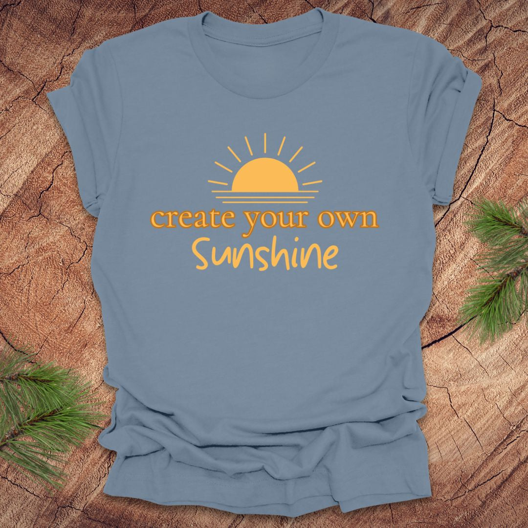 Light blue t-shirt with 'create your own Sunshine' text and sun graphic on a wooden surface.