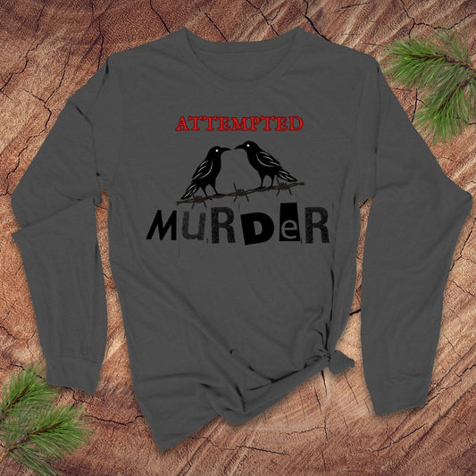 Dark gray long-sleeve shirt with 'ATTEMPTED MURDER' and crow design on a wooden surface.