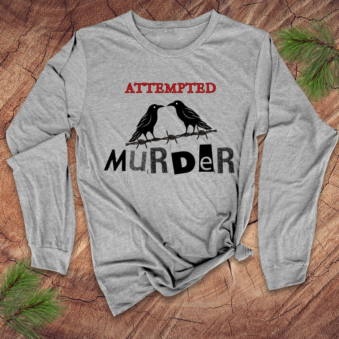 Gray long-sleeve shirt with 'ATTEMPTED MURDER' and crowdesign on a wooden surface
