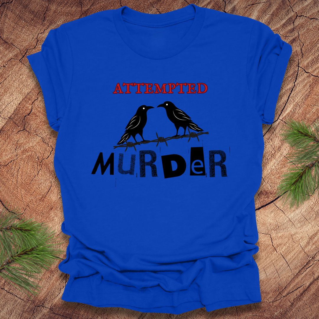 Royal blue t-shirt with black and red text 'Attempted Murder' and crows on a wooden surface.
