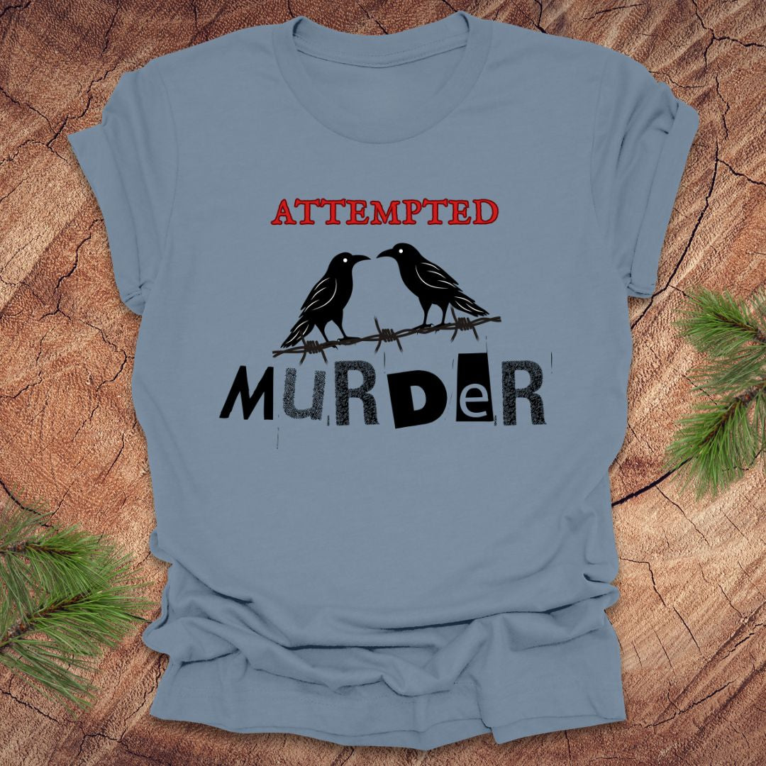 Steel blue t-shirt with black and red text 'Attempted Murder' and crows on a wooden surface.