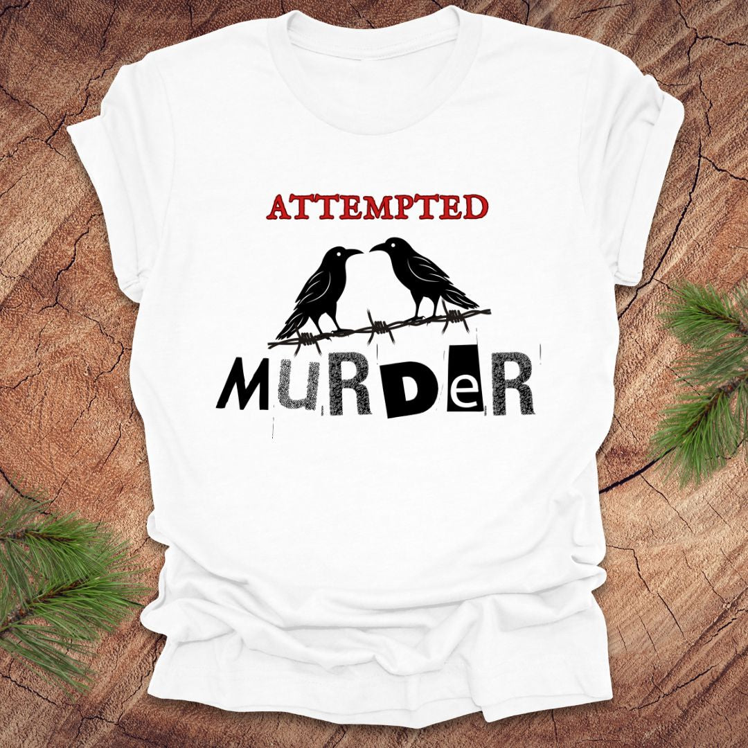 White t-shirt with black and red text 'Attempted Murder' and crows on a wooden surface.