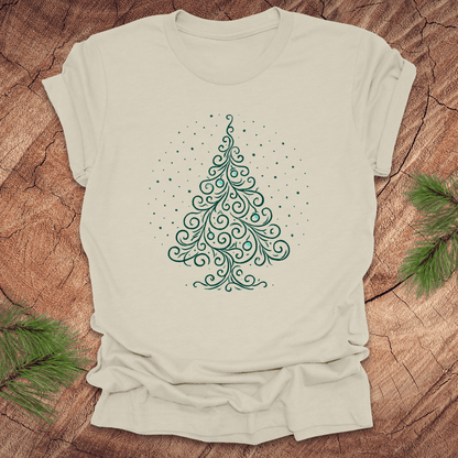 Beige t-shirt with a green Christmas tree design on a wooden surface with pine branches.