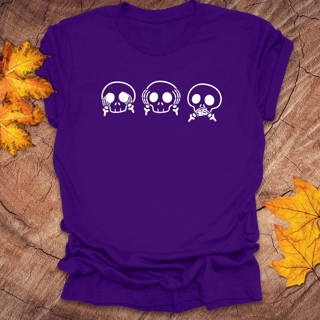 Purple tshirt with 3 skulls simulating see no evil, hear no evil, speak no evil, on a wood background with fall leaves.