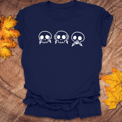 Navy tshirt with 3 skulls simulating see no evil, hear no evil, speak no evil, on a wood background with fall leaves.