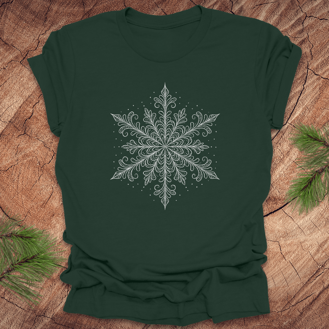 Forest Green t-shirt with a white snowflake design on a wooden surface with pine branches.