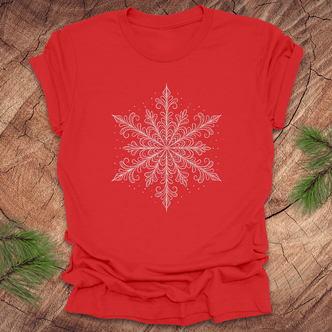 Red t-shirt with a white snowflake design on a wooden surface with greenery.