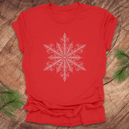 Red t-shirt with a white snowflake design on a wooden surface with greenery.
