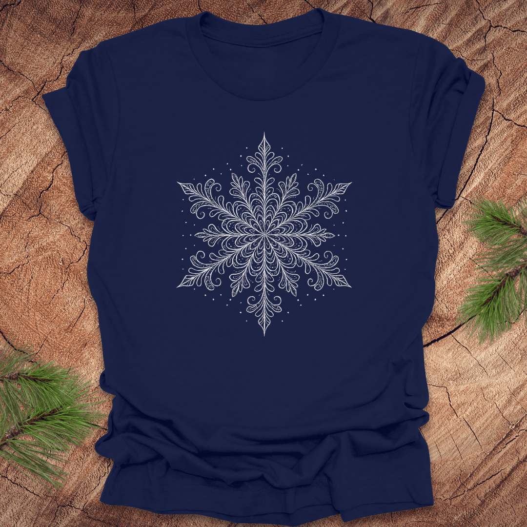 Navy blue t-shirt with a white snowflake design on a wooden surface with pine branches.