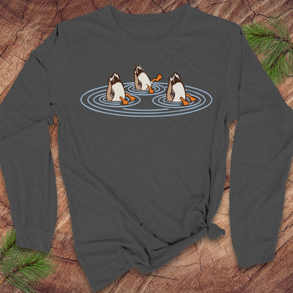 Asphalt gray long-sleeve t-shirt with three Mallards dabbling bottoms-up in rippling pond water, laid flat on a rustic wood background with pine branches.
