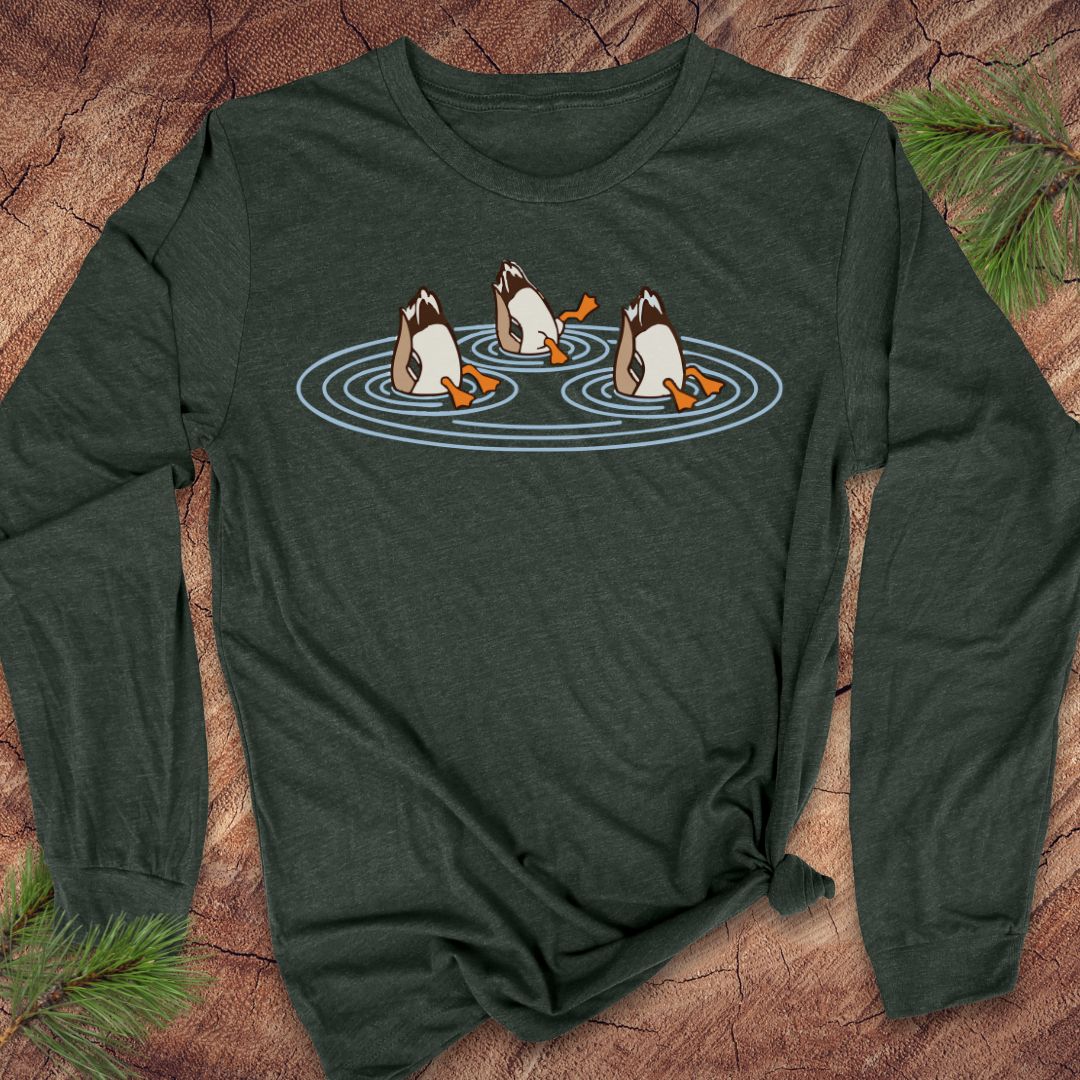 Heather forest green long-sleeve t-shirt with three Mallards dabbling bottoms-up in rippling pond water, laid flat on a rustic wood background with pine branches.
