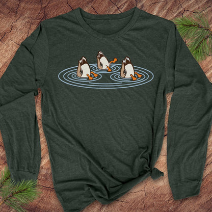 Heather forest green long-sleeve t-shirt with three Mallards dabbling bottoms-up in rippling pond water, laid flat on a rustic wood background with pine branches.