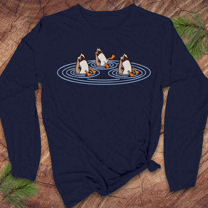 Navy long-sleeve t-shirt with three Mallards dabbling bottoms-up in rippling pond water, laid flat on a rustic wood background with pine branches.