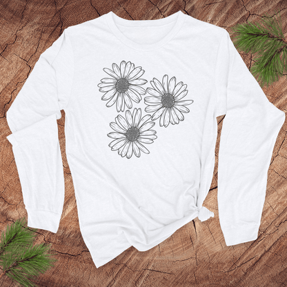 A white long-sleeve tshirt with 3 large daisies on a wooden surface with pine branches