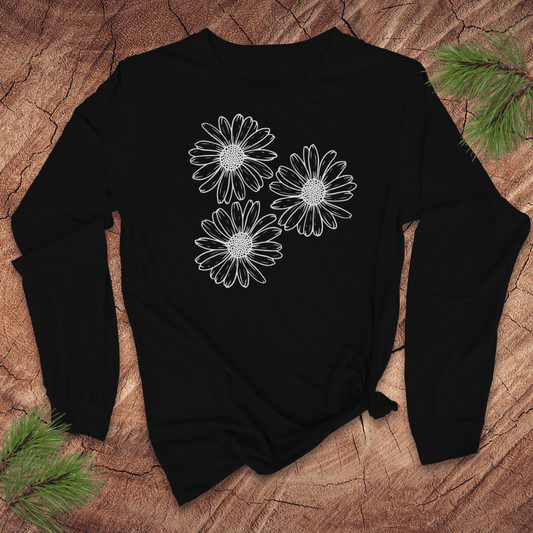 Black long-sleeve tshirt with 3 large daisies on a wooden surface with pine branches