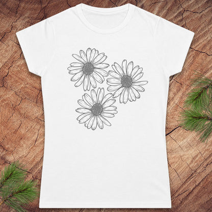 A white short-sleeve crewneck t-shirt featuring a black line art graphic of three daisy flowers on the front, displayed flat on a rustic wood background with pine branches in the corners.