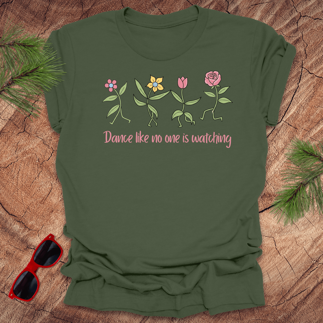 Green t-shirt with flower dancing design and text, 'Dance like no one is watching' on a wooden surface with sunglasses and greenery.
