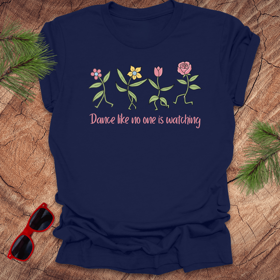 Navy blue t-shirt with flower dancing design and text, 'Dance like no one is watching' on a wooden surface with sunglasses and greenery.