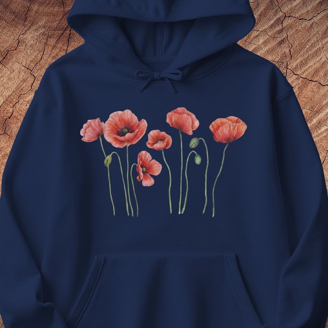 A navy blue pullover hoodie featuring a watercolor-style graphic of pink poppy flowers with green stems on the chest, displayed against a textured brown wood background.