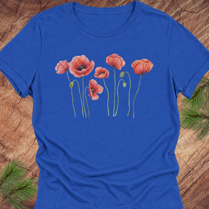 True royal blue women's relaxed t-shirt with watercolor red-orange poppies on slender green stems, laid flat on a rustic wood background with pine branches.