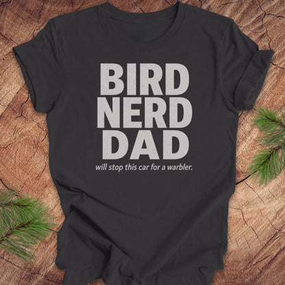 Gray t-shirt with 'BIRD NERD DAD' text on a wooden surface with pine branches.