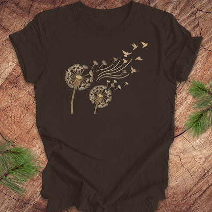 Brown t-shirt with dandelion and bird design on a wooden surface