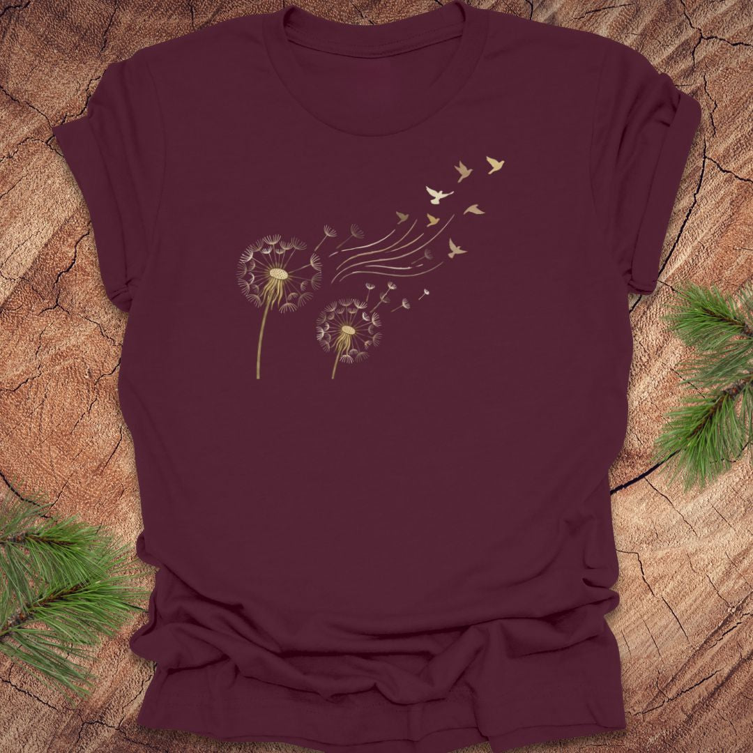 Maroon t-shirt with dandelion and bird graphic on a wooden surface