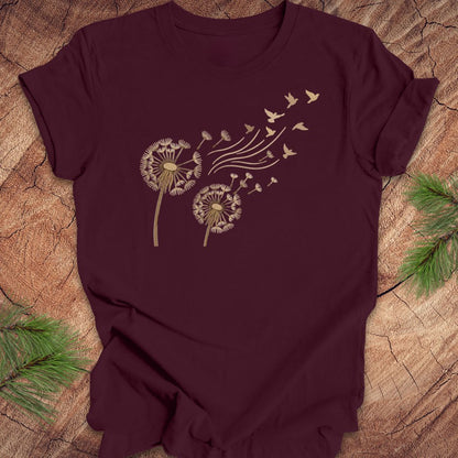 Maroon t-shirt with dandelion and bird design on a wooden surface