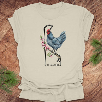 Beige t-shirt with a rooster design and 'Delaware' text on a wooden surface.