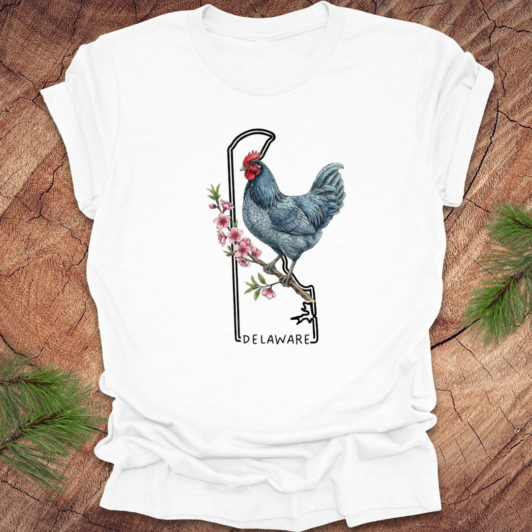 White t-shirt with a rooster design and 'Delaware' text on a wooden surface.