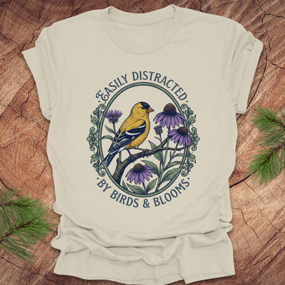 Beige t-shirt with a graphic of a bird and flowers on a wooden surface