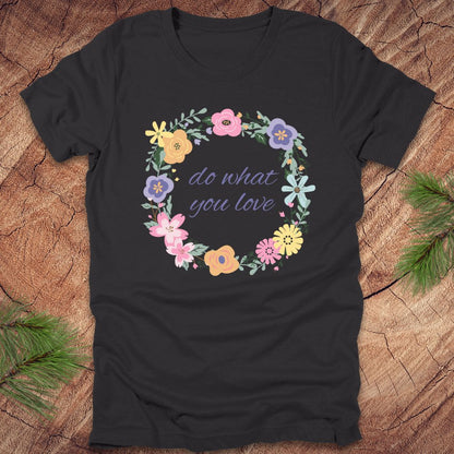 A Dark grey t-shirt with a floral wreath design and text, 'Do what you love' on a wood background.