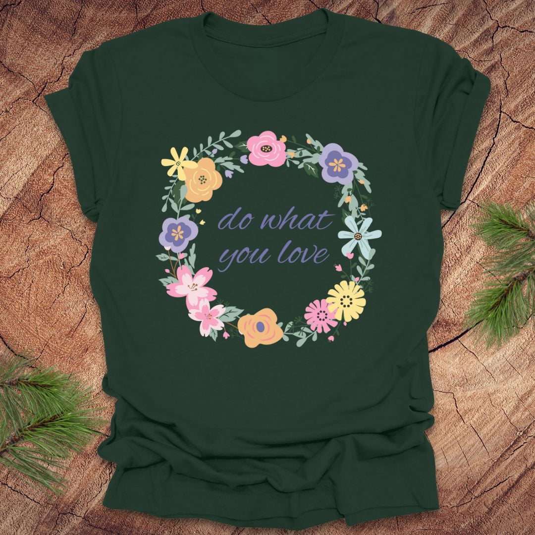 A forest green t-shirt with a floral wreath design and text, 'Do what you love' on a wood background.