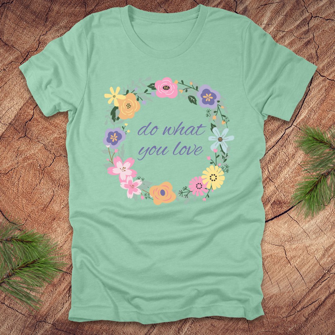 A Mint green t-shirt with a floral wreath design and text, 'Do what you love' on a wood background.