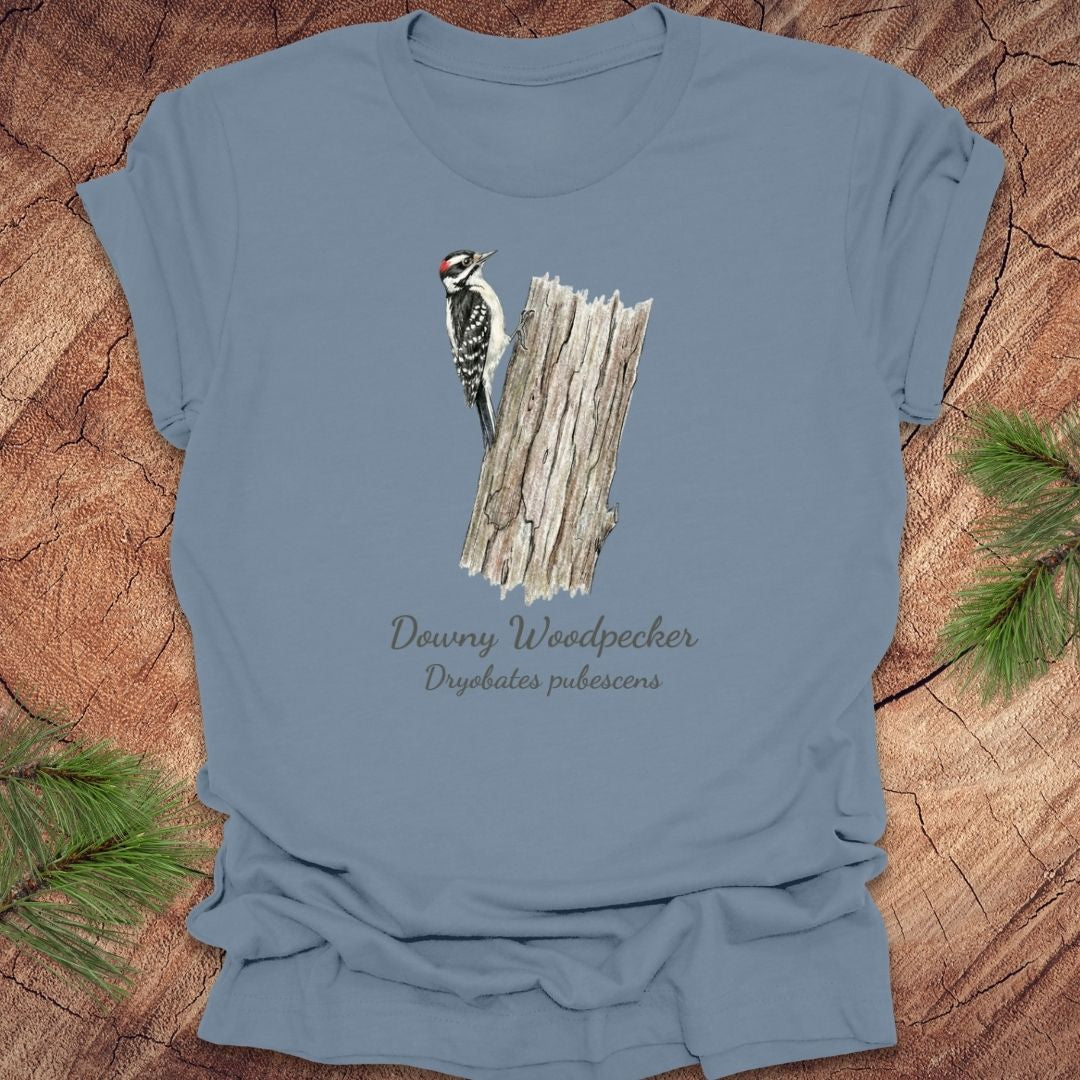 Steel blue t-shirt featuring a downy woodpecker perched on a tree with text, on a wood background.