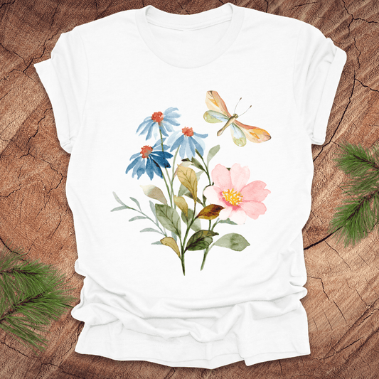 White t-shirt with floral design featuring flowers and a dragonfly on a wooden surface.