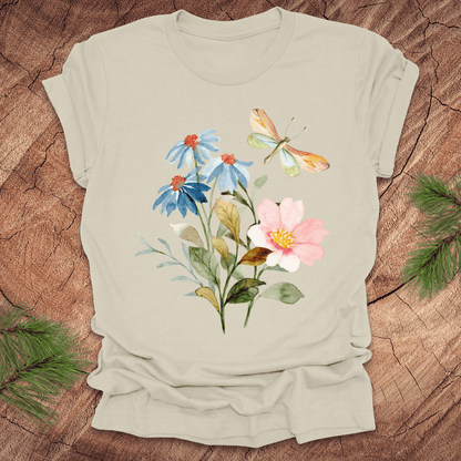 Beige t-shirt with floral design featuring flowers and a dragonfly on a wooden surface.