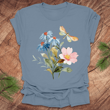 Blue t-shirt with floral design featuring flowers and a dragonfly on a wooden surface.