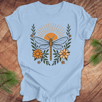 Blue t-shirt with a dragonfly, sunrise and flowers on a wood background.