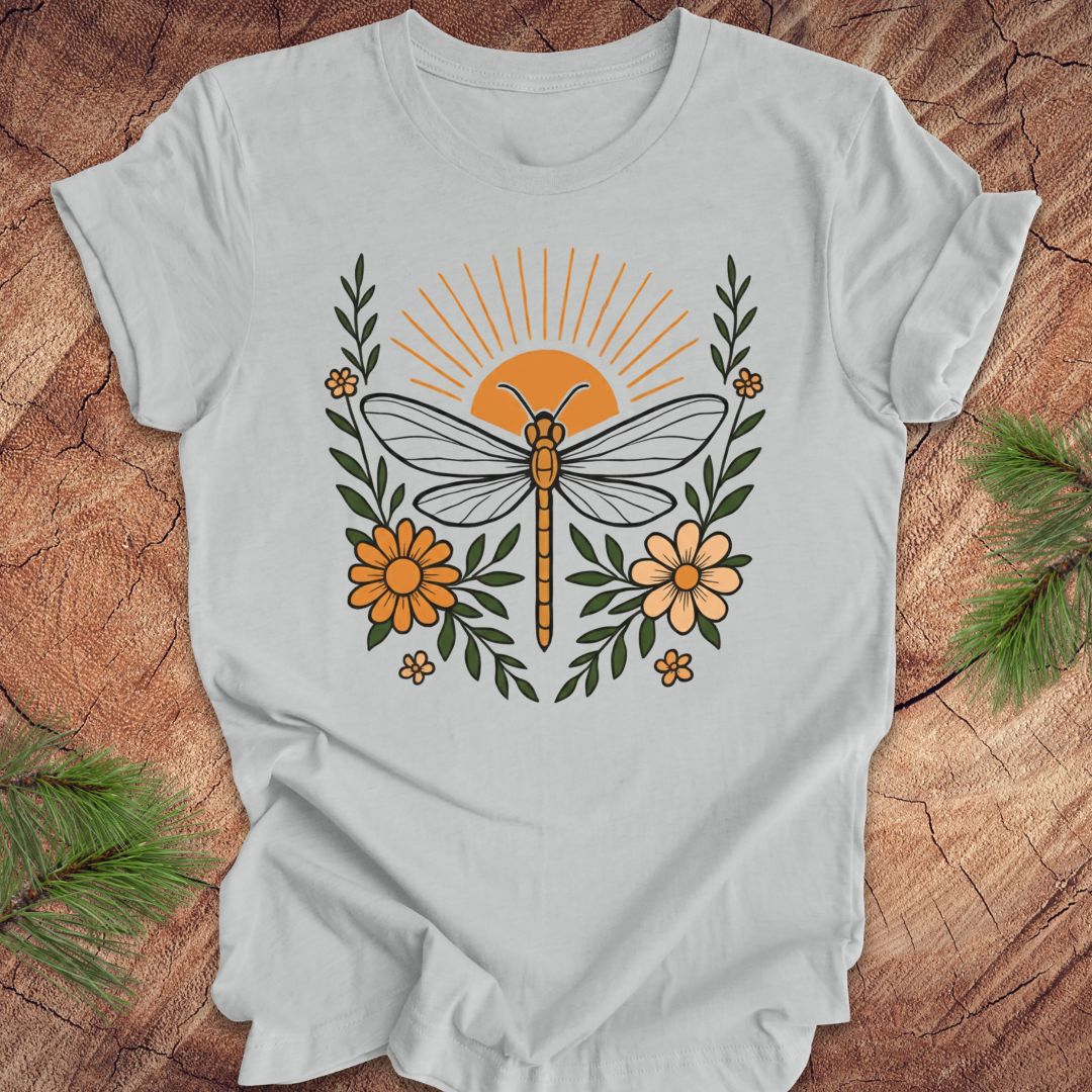 Gray t-shirt with a dragonfly, sunrise and flowers on a wood background.