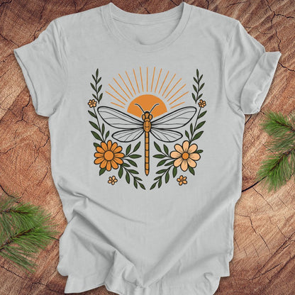 Gray t-shirt with a dragonfly, sunrise and flowers on a wood background.