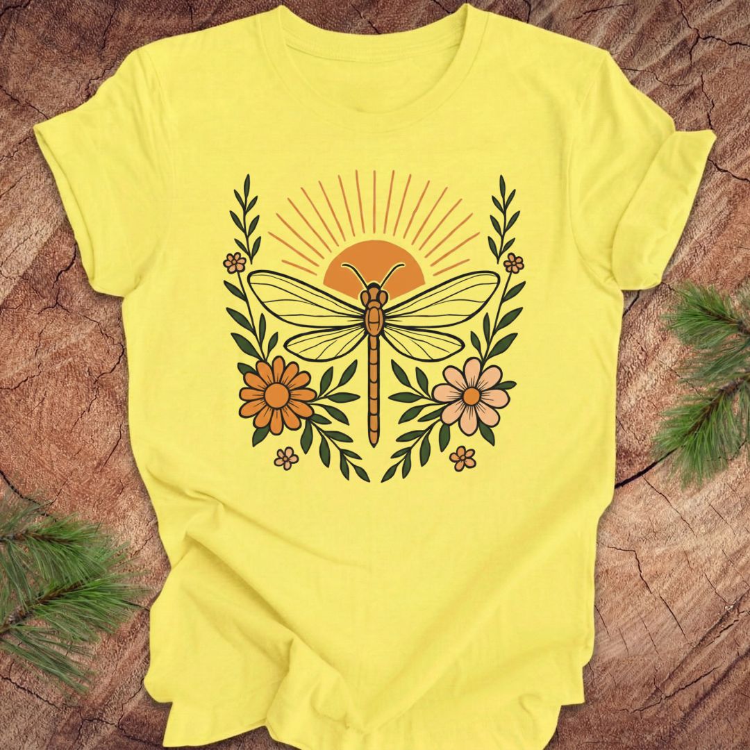 Yellow t-shirt with a dragonfly, sunrise and flowers on a wood background.