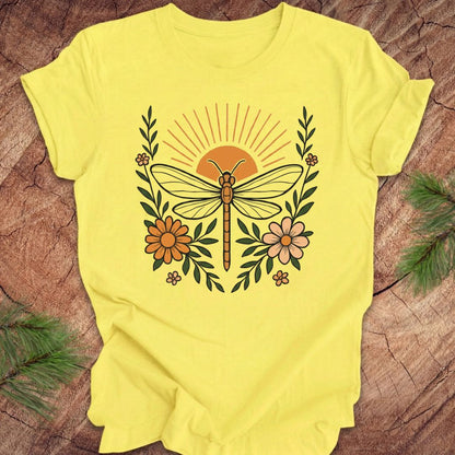 Yellow t-shirt with a dragonfly, sunrise and flowers on a wood background.
