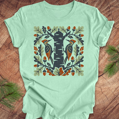 Mint green t-shirt with folk art woodpeckers in a tree design on a wooden surface