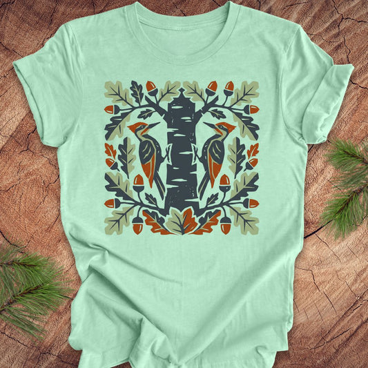Mint green t-shirt with folk art woodpeckers in a tree design on a wooden surface