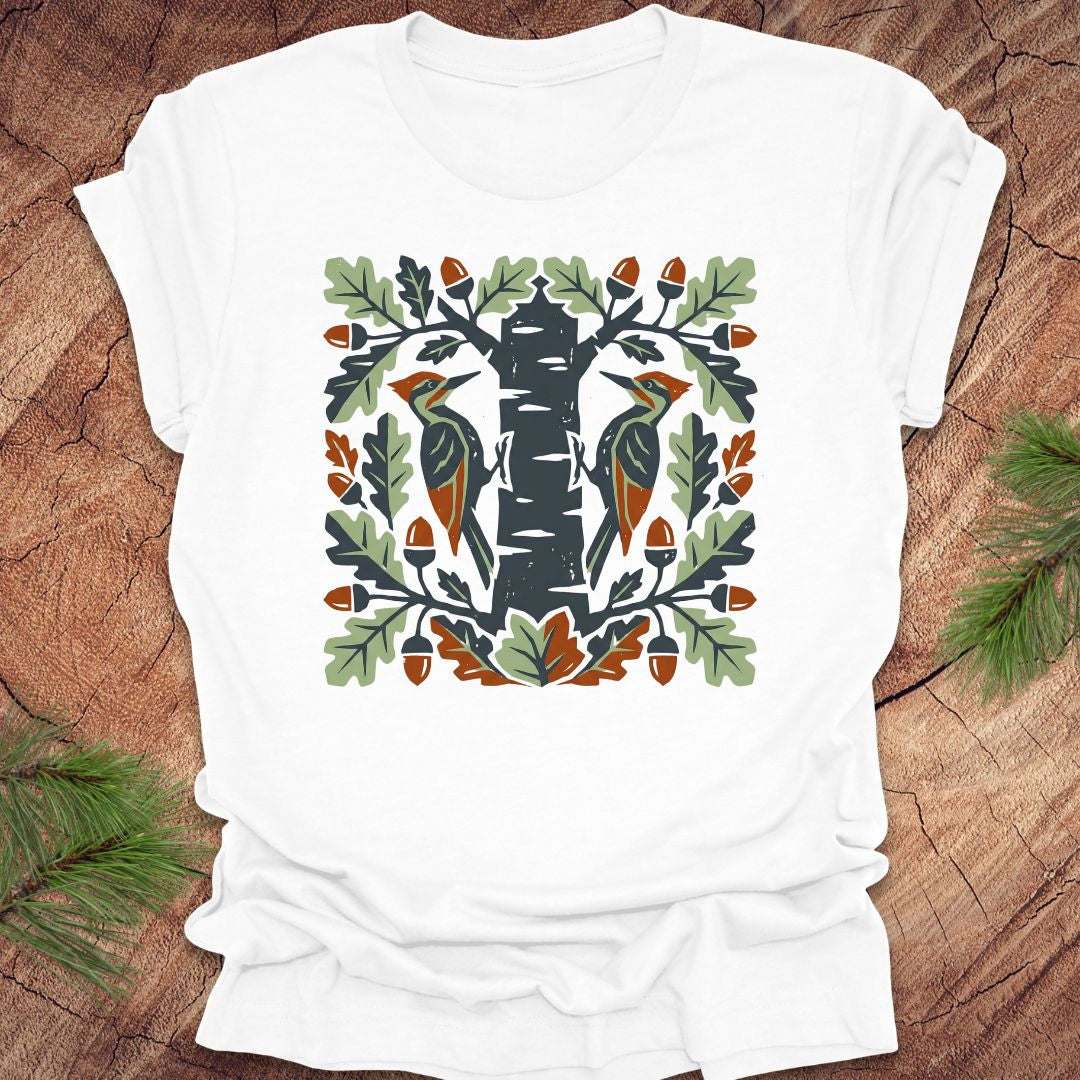 White t-shirt with folk art woodpeckers in a tree design on a wooden surface