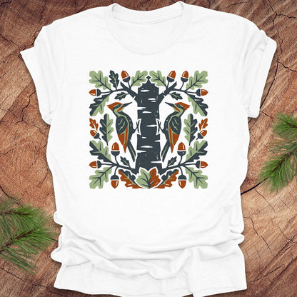 White t-shirt with folk art woodpeckers in a tree design on a wooden surface