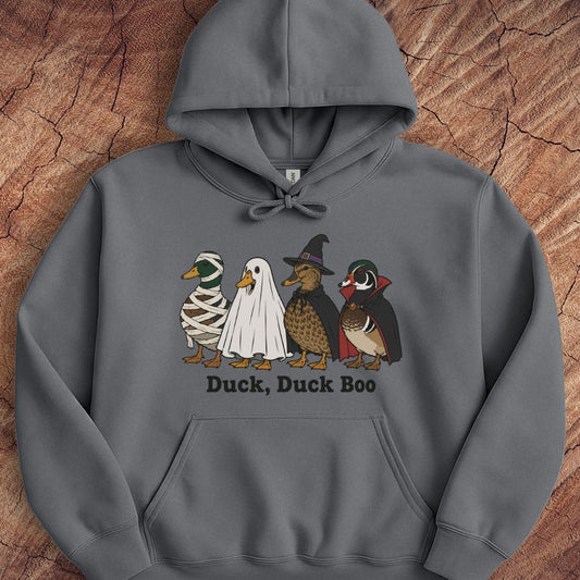 A dark gray pullover hoodie laid flat on a textured wood background, featuring a graphic of four cartoon ducks in Halloween costumes with the text 'Duck, Duck Boo' printed below.